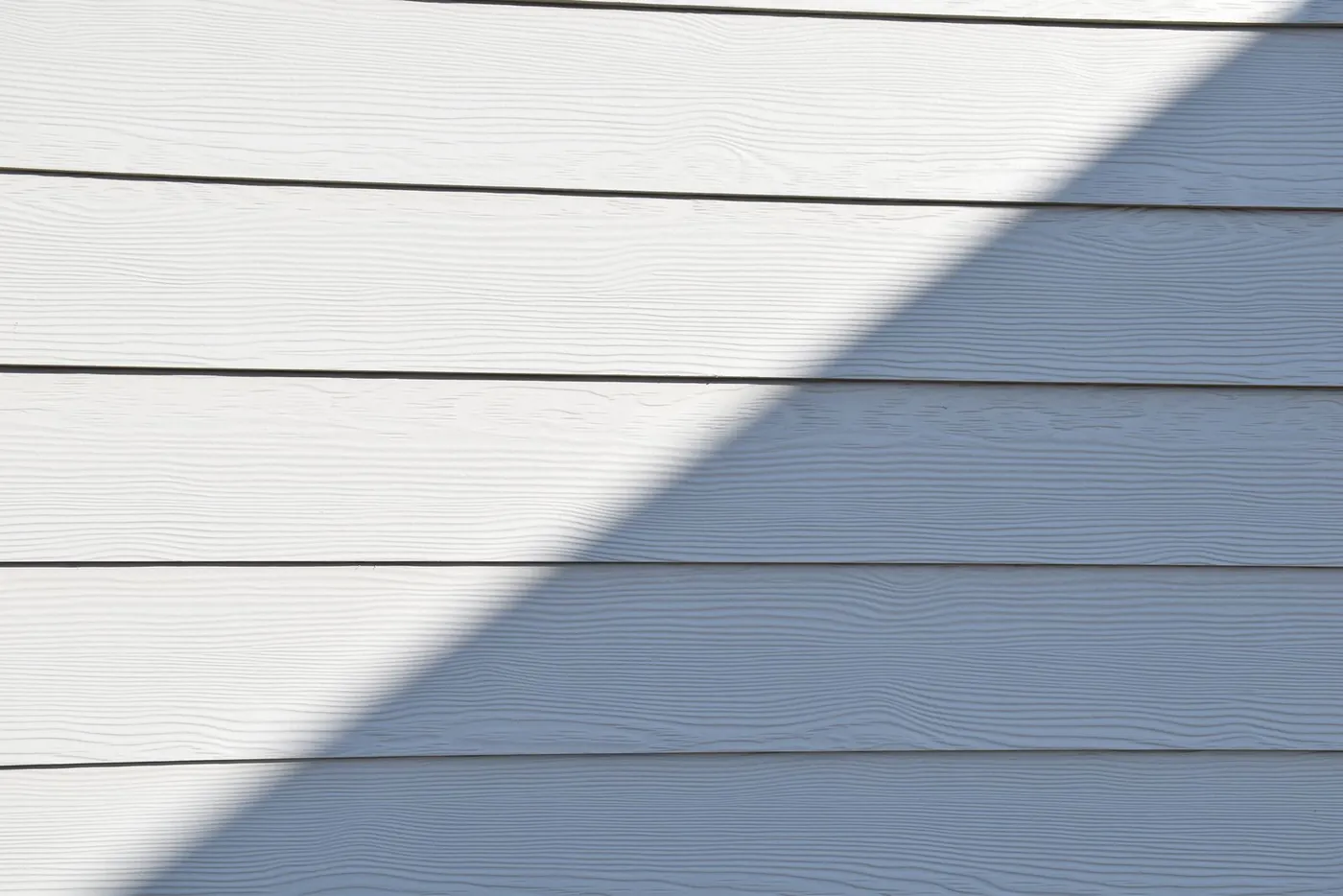 White fiber cement lap siding with a woodgrain texture, half of it in hard shadow