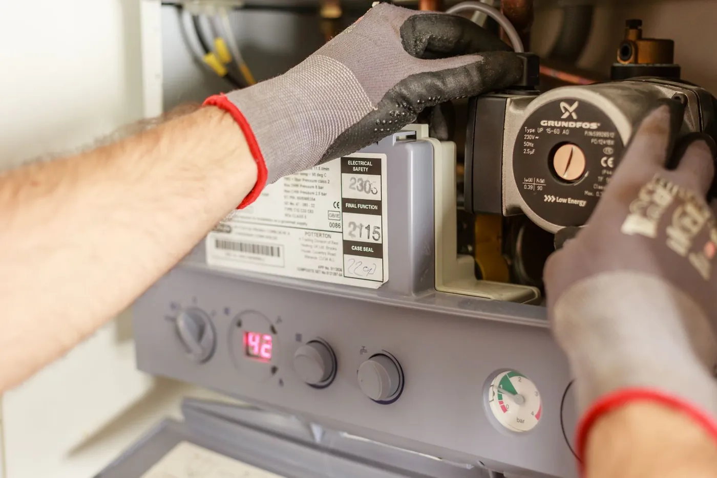 Gloved hands servicing a wall-hung gas water-heating unit